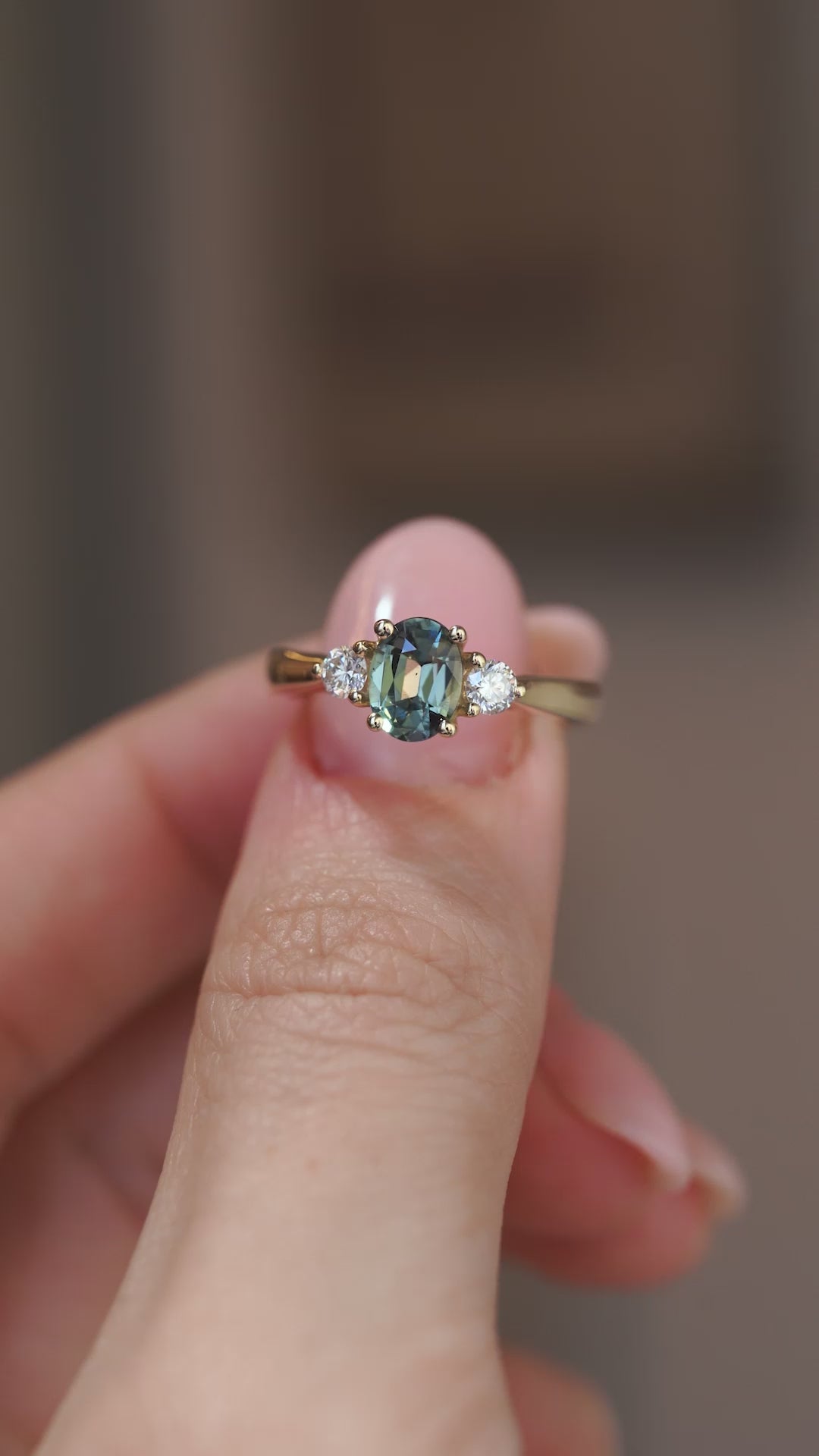 A close-up video of the sapphire engagement ring held between fingers, showcasing the gemstone's colour and diamond shoulders.