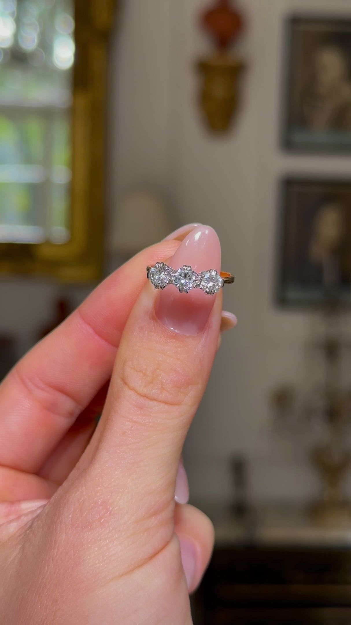 three stone diamond engagement ring, held in fingers and rotated to give perspective,front view.