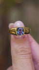 A close-up of an antique Victorian colour-change sapphire gypsy ring held between the fingers showing green, blue and purple hues in video.