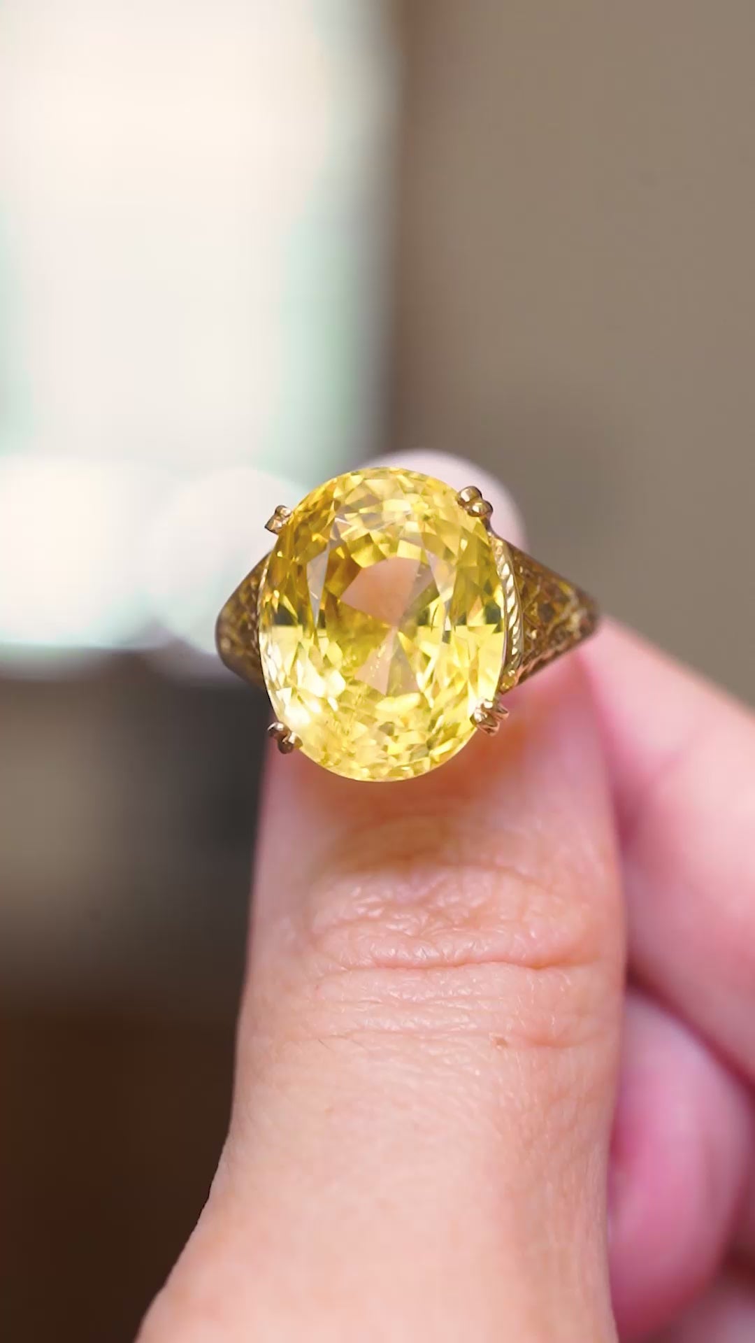 A vintage, sunshine-yellow sapphire cocktail ring in yellow gold held between fingers showing the details of the ring. 