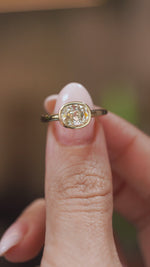Video close-up of an antique-inspired diamond solitaire balanced on a fingertip, displaying the old-mine cut and polished gold surround.