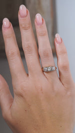 A close-up video of an antique Edwardian diamond three-stone engagement ring modelled on a hand, highlighting the old-cut diamonds, platinum setting and polished yellow gold band.