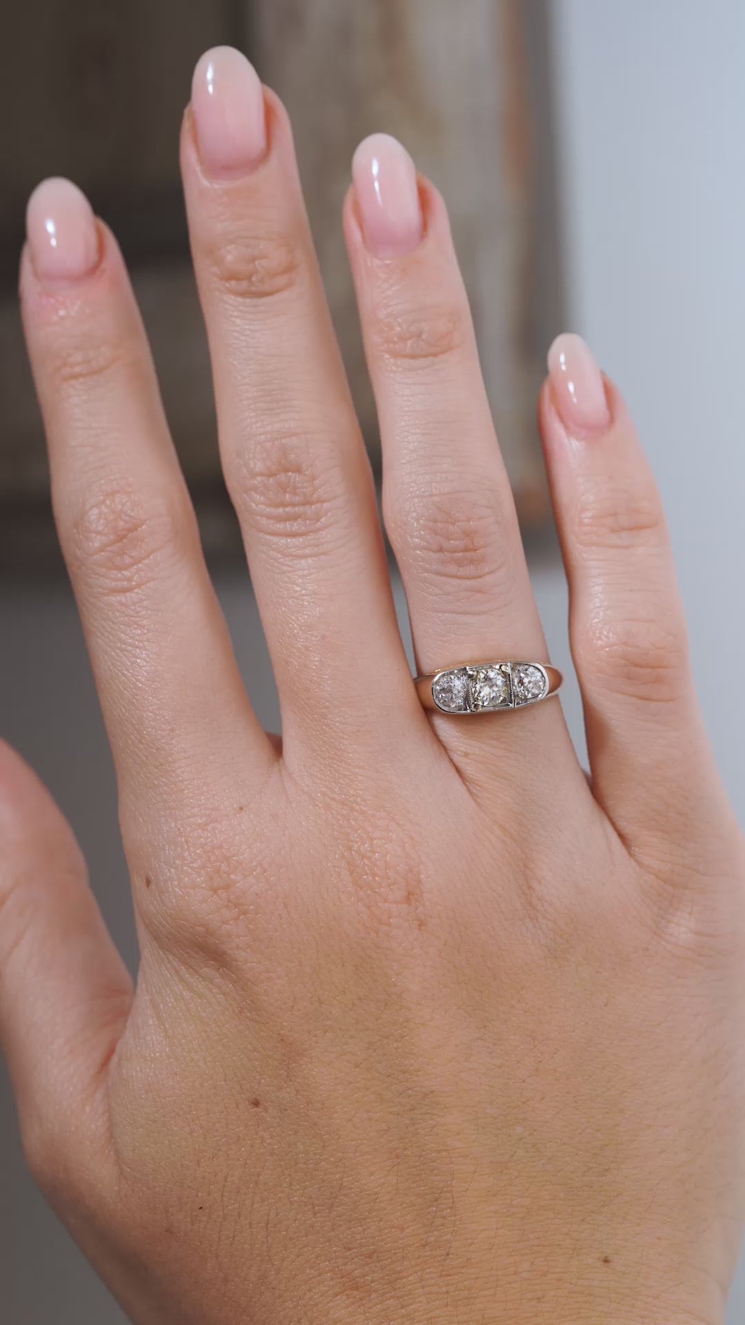 A close-up video of an antique Edwardian diamond three-stone engagement ring modelled on a hand, highlighting the old-cut diamonds, platinum setting and polished yellow gold band.