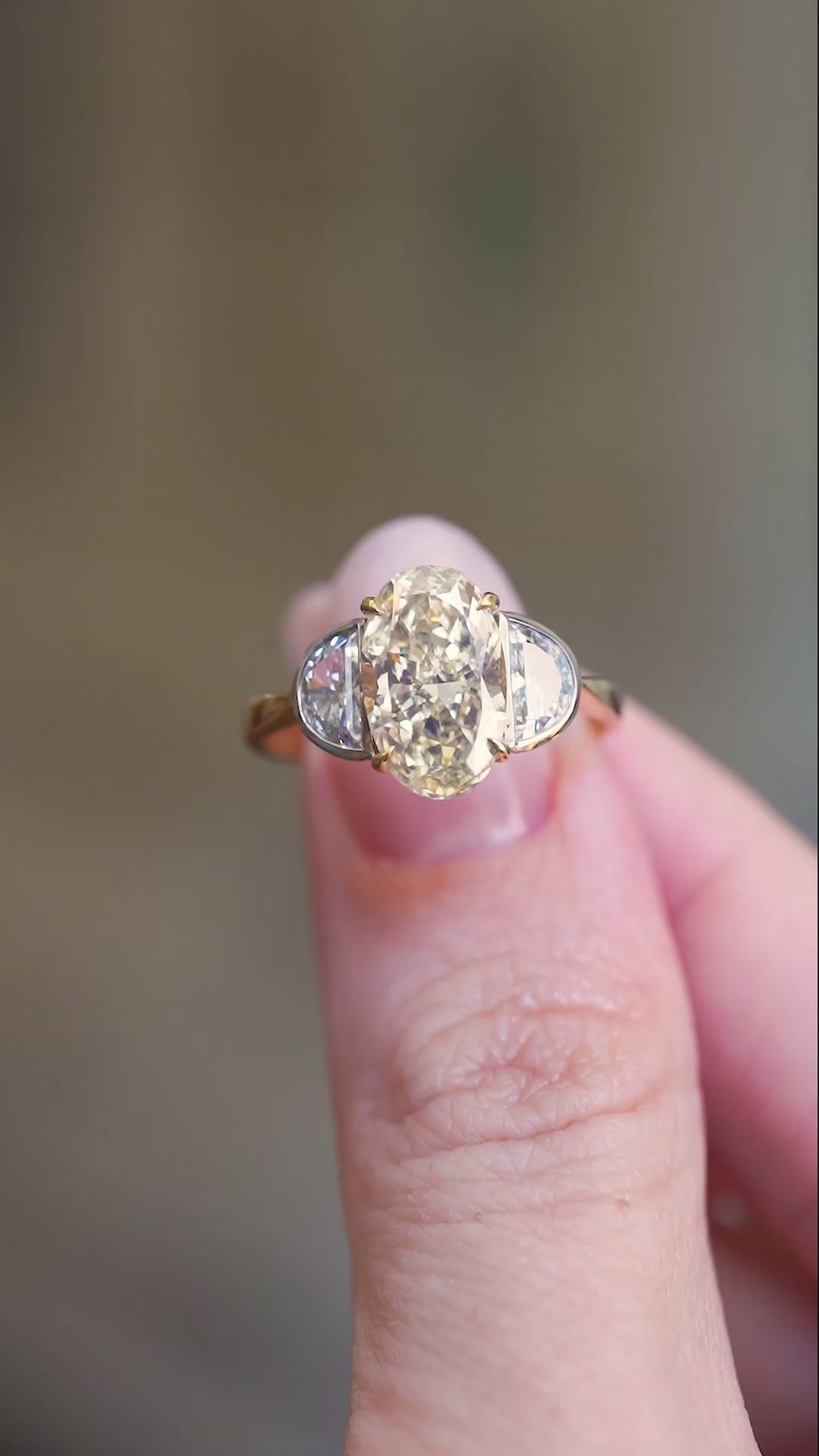 Vintage yellow oval diamond and half-moon diamond three-stone ring shown in motion between fingers.