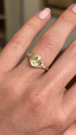 Video of a Vintage-inspired yellow cushion-cut sapphire & diamond engagement ring worn on an engagement finger and slowly rotated to display the angles of the ring. 