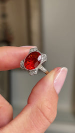 Antique Art Deco fire opal and diamond cluster ring featuring a fiery orange-red opal encircled by diamonds, held by hand for detailed viewing.