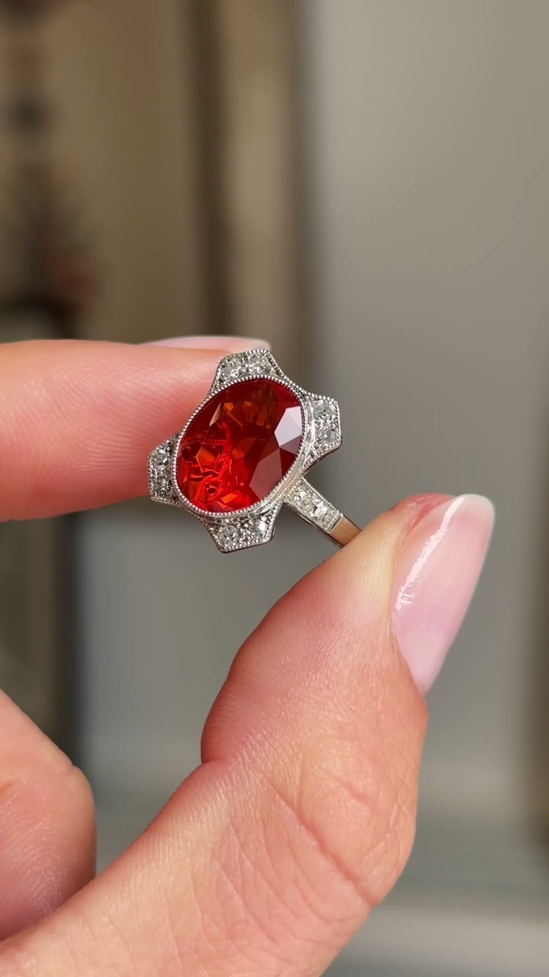 Antique Art Deco fire opal and diamond cluster ring featuring a fiery orange-red opal encircled by diamonds, held by hand for detailed viewing.