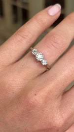 A close up video of a vintage three-stone old-cut diamond engagement ring in white gold worn on a wedding finger. 