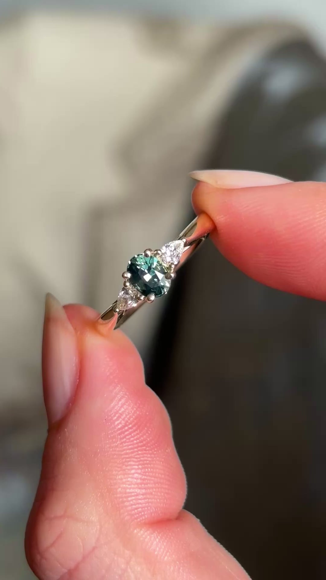 Oval-cut teal sapphire and diamond three-stone engagement ring captured in natural light, highlighting the sparkle and colour of the gemstones.