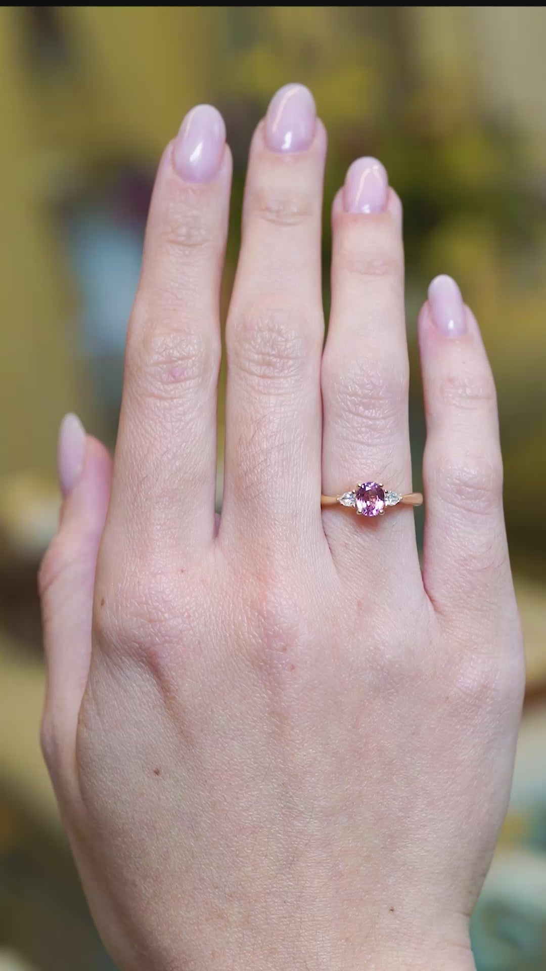 Pink sapphire and diamond three-stone engagement ring shown in slow movement on hand.