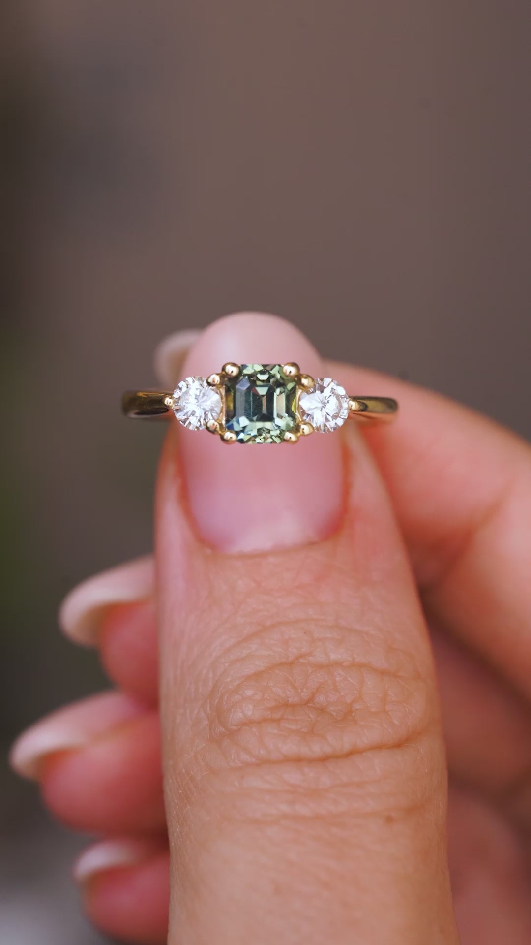 a video of an Antique-inspired, Teal sapphire and diamond three-stone engagement ring in yellow gold held between fingers and rotated to show different angles.