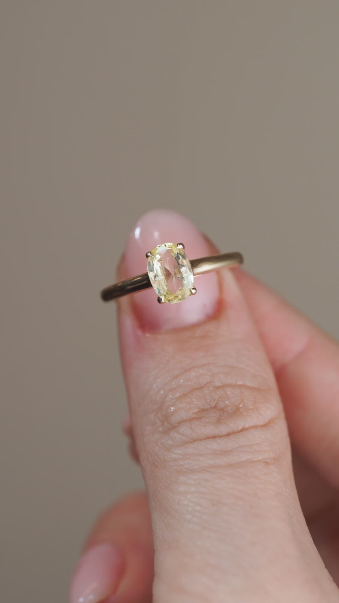 A video showing the sapphire solitaire held between fingers, revealing the pale golden hues and natural facets of the centre stone.