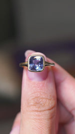 A video of a yellow gold antique-inspired blue sapphire solitaire ring held in between the fingers and turned to showcase different angles against a blurry background.