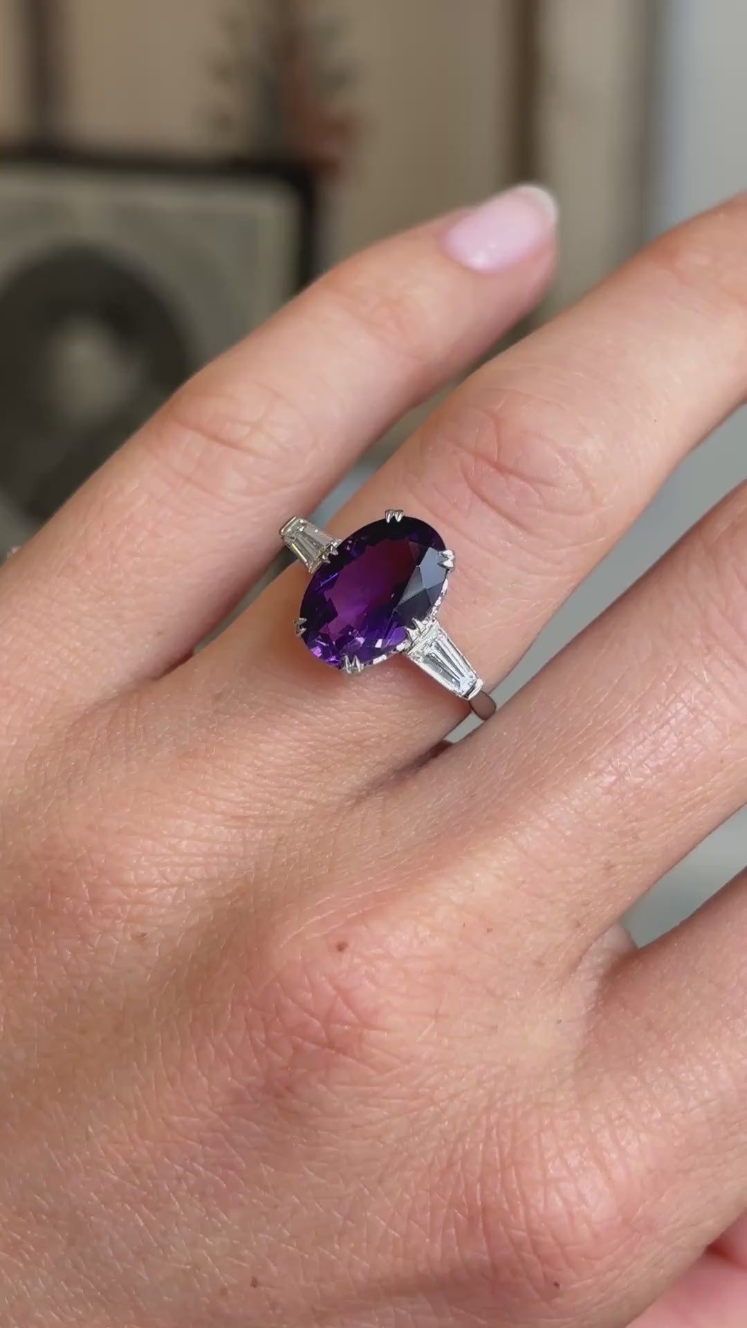 Antique Art Deco three-stone ring in platinum worn on hand, featuring a richly coloured purple amethyst flanked by baguette diamonds, filmed against a softly lit vintage interior backdrop.
