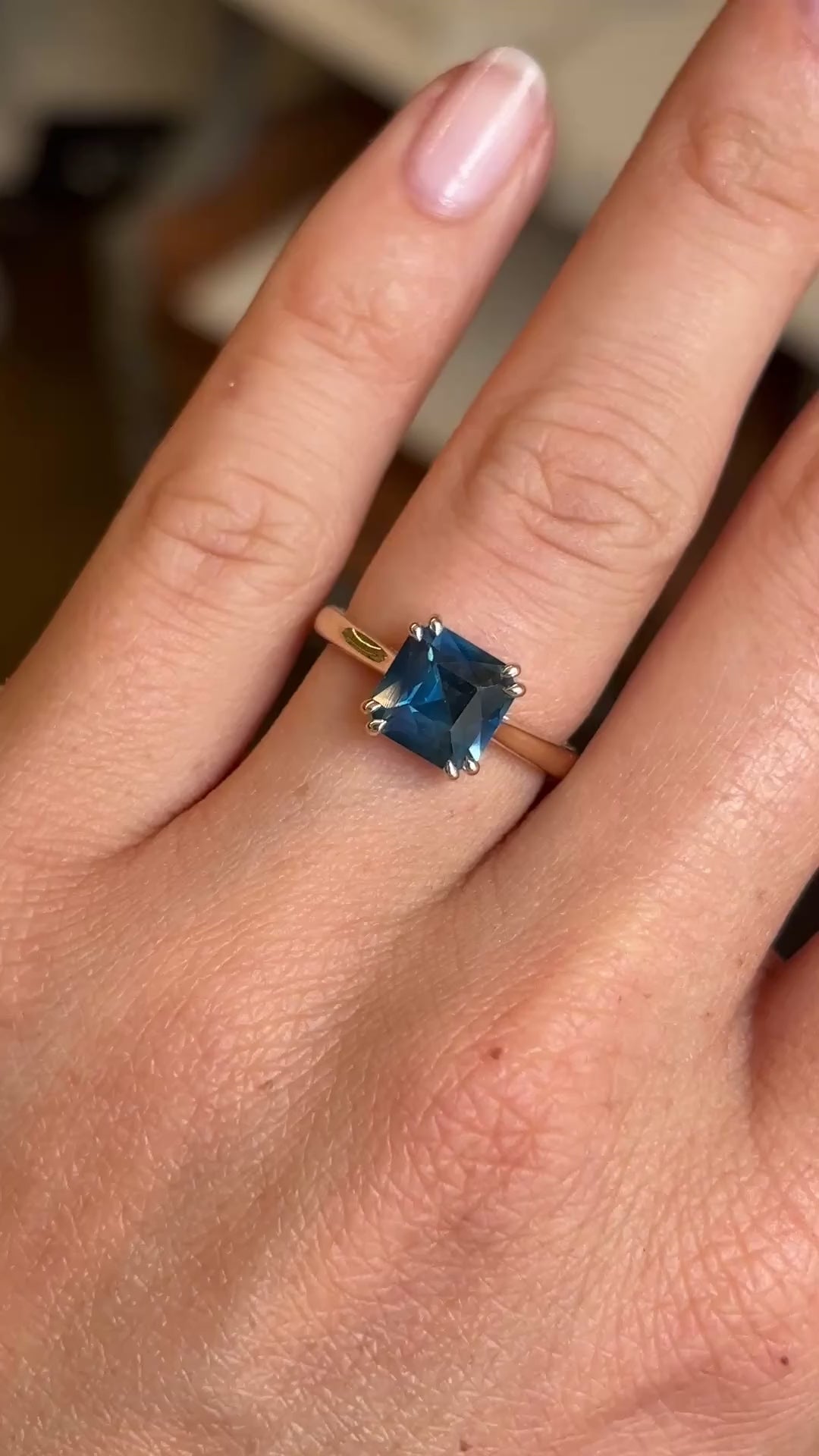 A close up video of an Antique-inspired, blue square-cut sapphire solitaire engagement ring in gold worn on a wedding finger. 