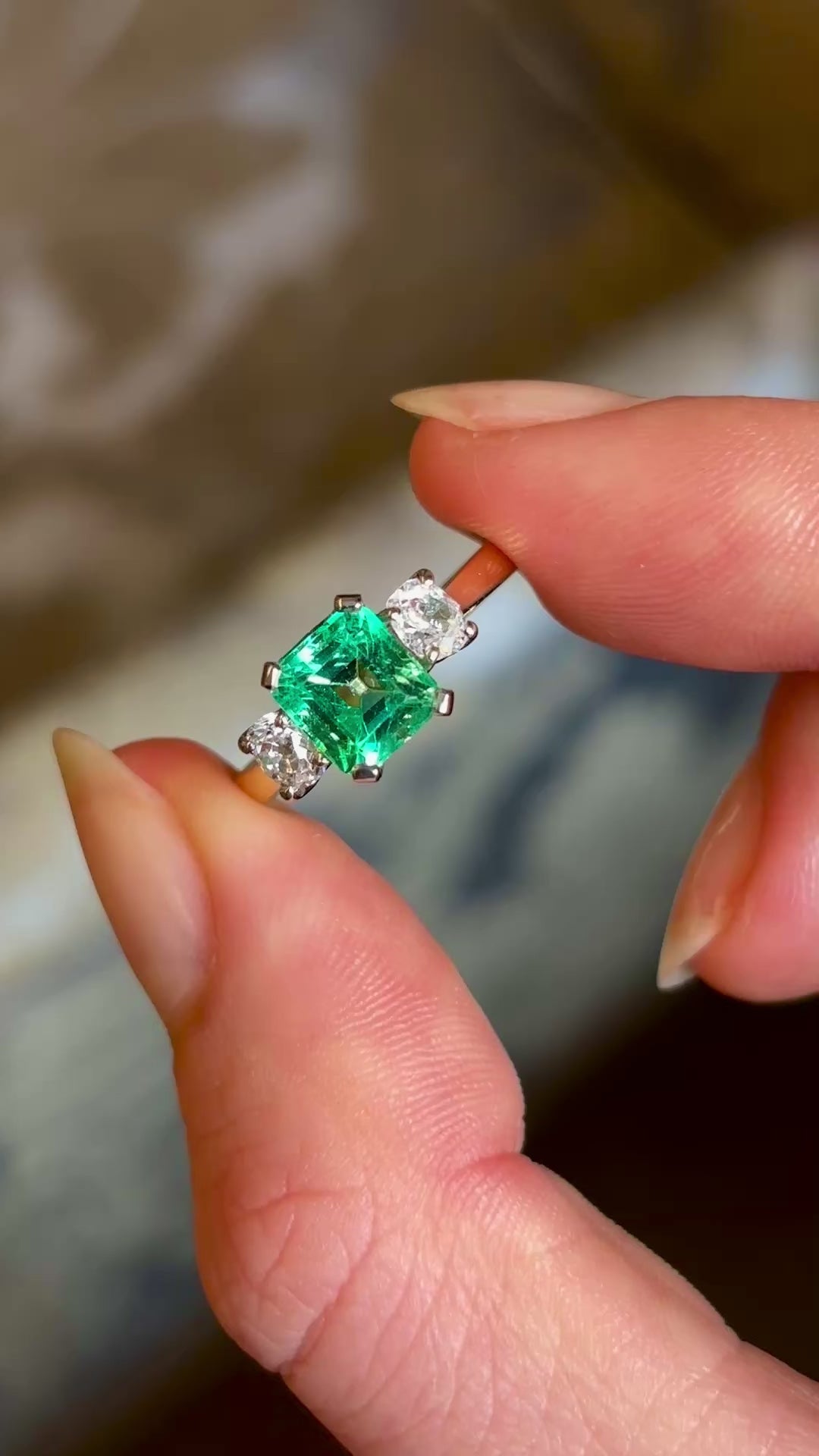 Vintage, emerald and diamond three-stone engagement ring held in fingers and rotated. 