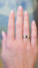 Antique five stone ring worn on hand with blue sapphire and old mine cut diamonds.
