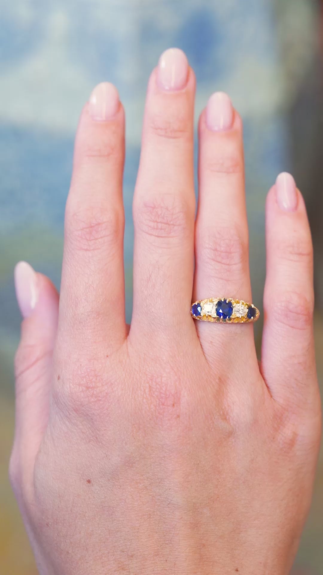 Antique five stone ring worn on hand with blue sapphire and old mine cut diamonds.