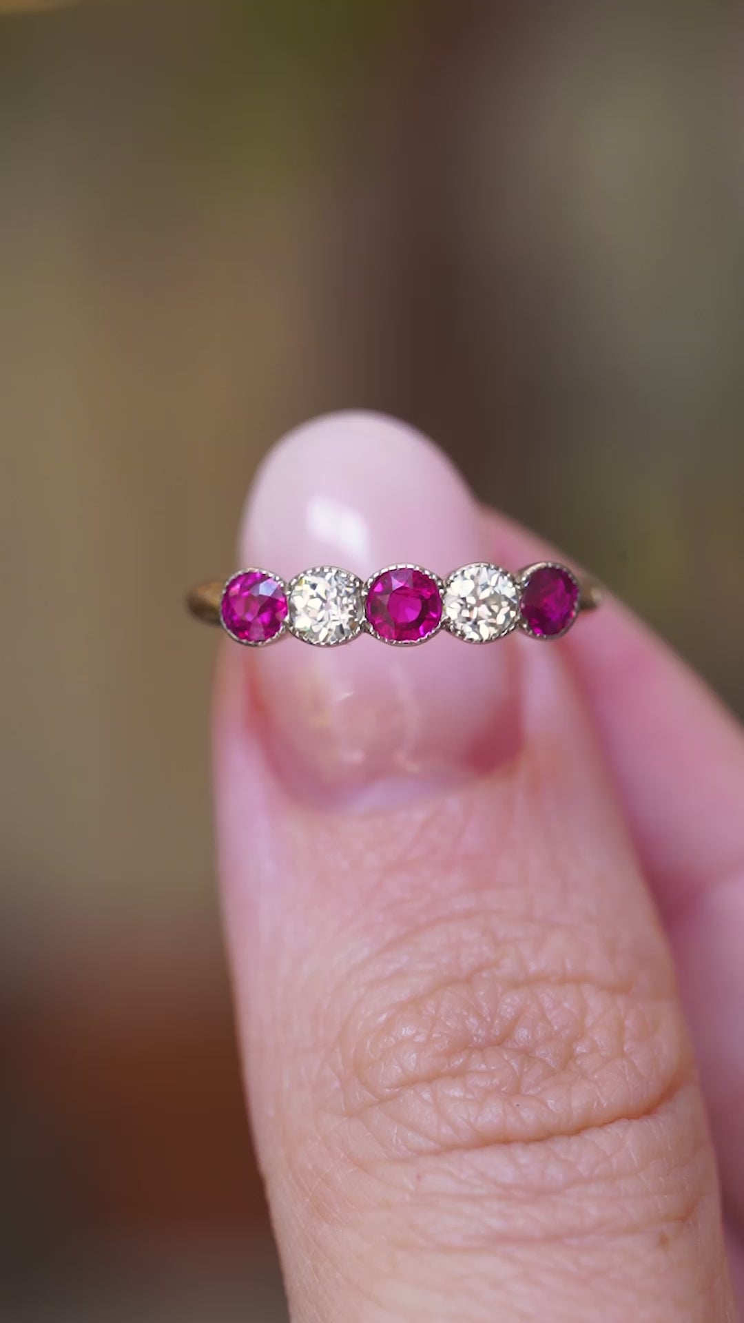 A video of an antique Edwardian ruby and old-cut diamond five-stone ring held between fingers.