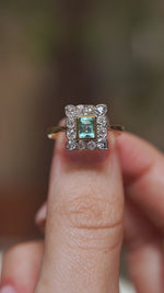 Video close-up of an antique mint green emerald engagement ring balanced on a fingertip, highlighting its old-mine cut diamond surround.