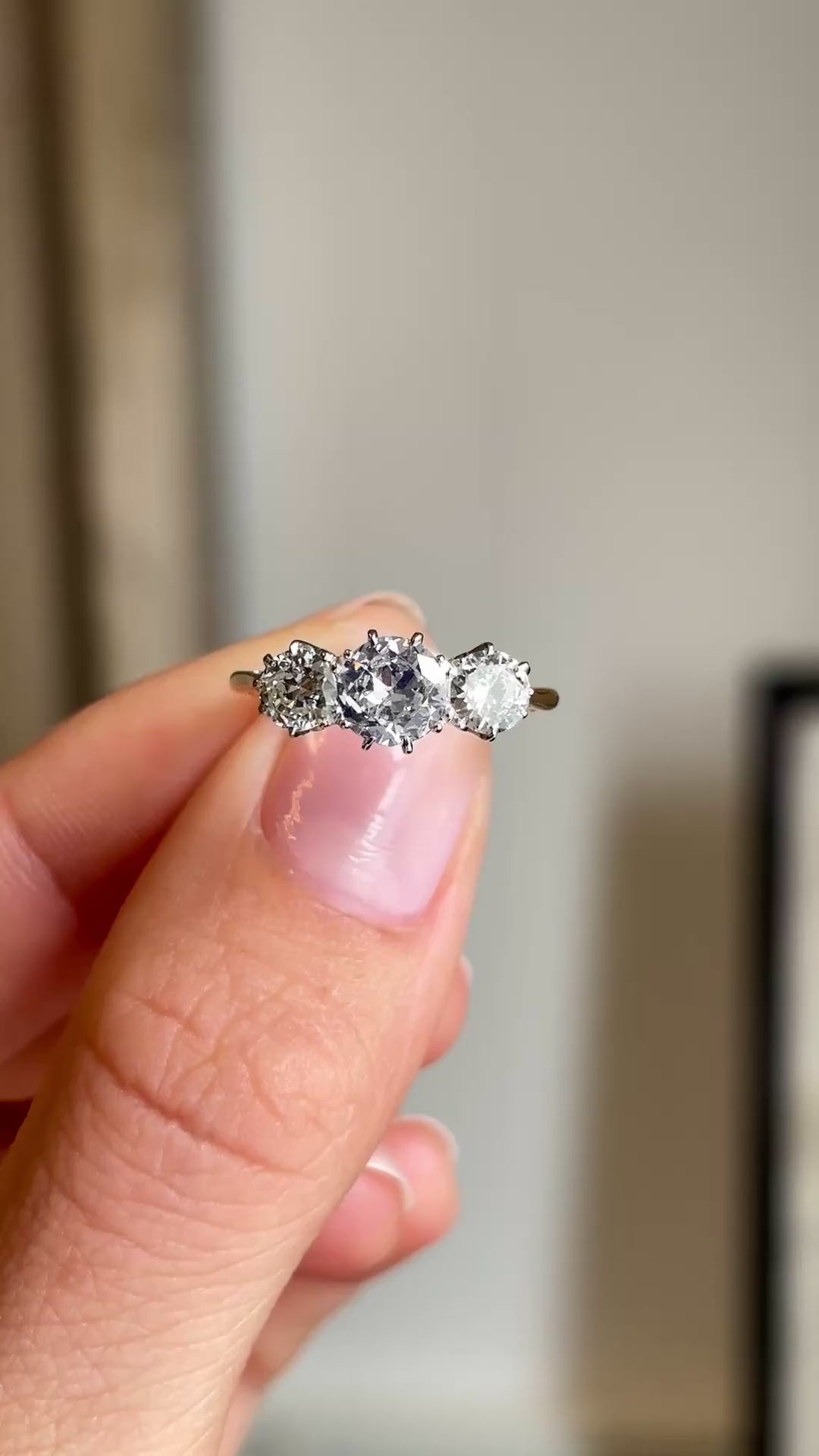 Close up video of a three-stone diamond engagement ring from the Edwardian era.  Held between two fingers and rotated slowly to showcase the profile of the ring and the yellow gold band
