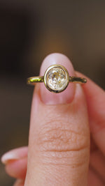 A close up video of an Antique-inspired, pale yellow sapphire solitaire engagement ring held between two fingers and rotated slower to showcase the yellow gold rub-over setting and band. 