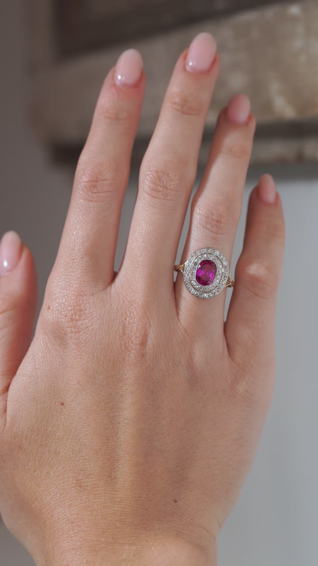 A close-up video of an antique Edwardian Burmese ruby and diamond cluster engagement ring modelled on a hand, showcasing the vivid ruby and sparkling double diamond surround.