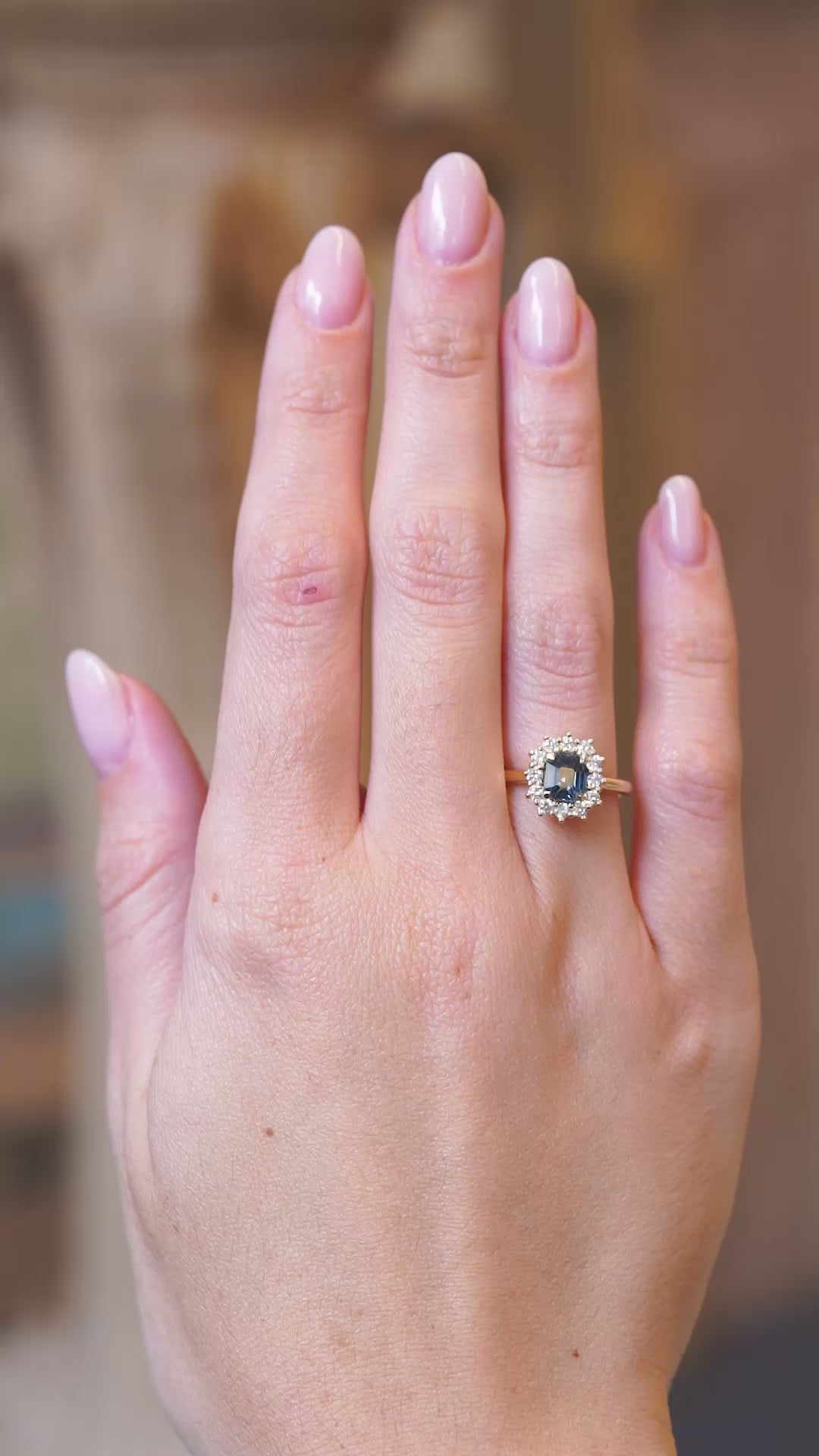 Teal sapphire and diamond cluster engagement ring worn on hand in motion.
