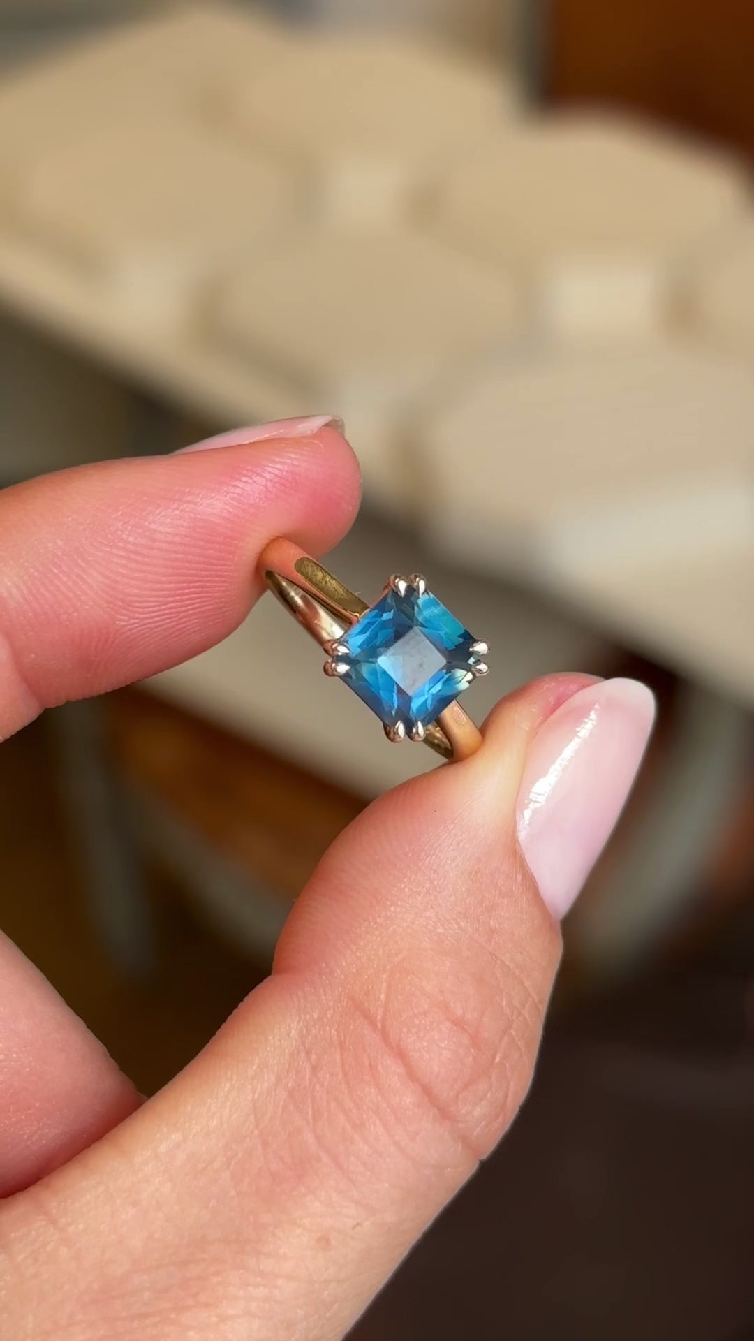 A video of an Antique-inspired, teal square-cut sapphire solitaire engagement ring in yellow gold held between two fingers and rotated slowly to display all profiles of the ring