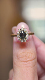 A video of a close-up of an antique-inspired yellow gold engagement ring featuring a green sapphire surrounded by a diamond cluster.