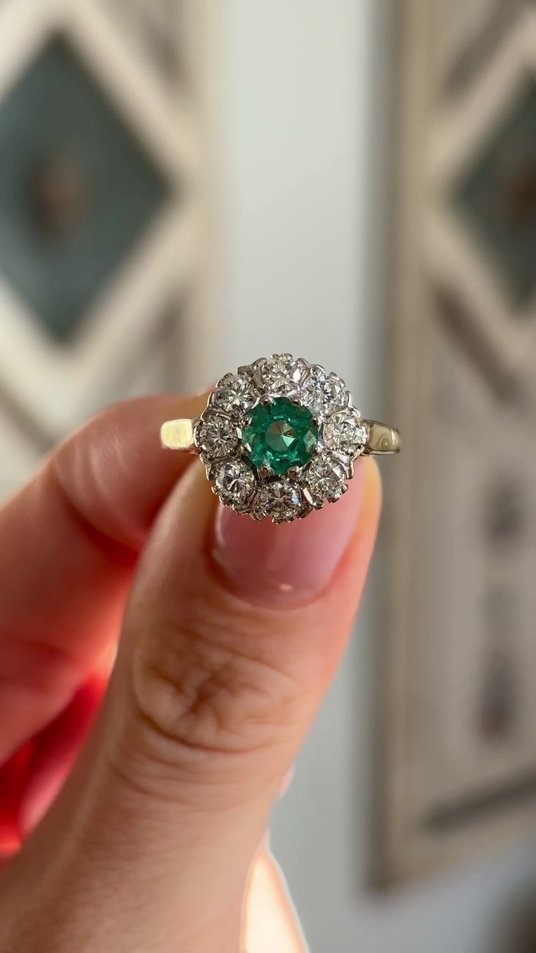 Vintage, 1980s emerald & diamond cluster ring held in fingers.