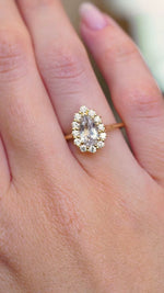 A video of a vintage-inspired white sapphire and diamond cluster engagement ring in yellow gold worn on the hand.