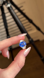 A video of a blue sapphire and diamond platinum ring held in between the fingers and slowly turned against a blurred background.