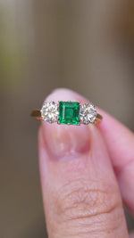 A video of a vintage 1960s emerald and diamond three-stone ring held between the fingers showing the details of the ring.