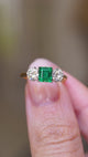A video of a vintage 1960s emerald and diamond three-stone ring held between the fingers showing the details of the ring.