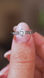 A close up video of an Antique, 1930s Art-Deco diamond flanked solitaire engagement ring in platinum.  Held between two fingers and rotated slowly to display the profile of the ring.
