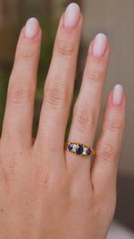 A video of an Antique, Edwardian five-stone engagement ring in yellow gold being worn on a wedding finger and rotated slowly to showcase the blue sapphires and diamonds and side profile of the ring. 