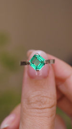 A close up video of a hand holding a Vintage, 1990s emerald solitaire engagement ring rotated slowly to showcase the profile, setting and white gold band. 
