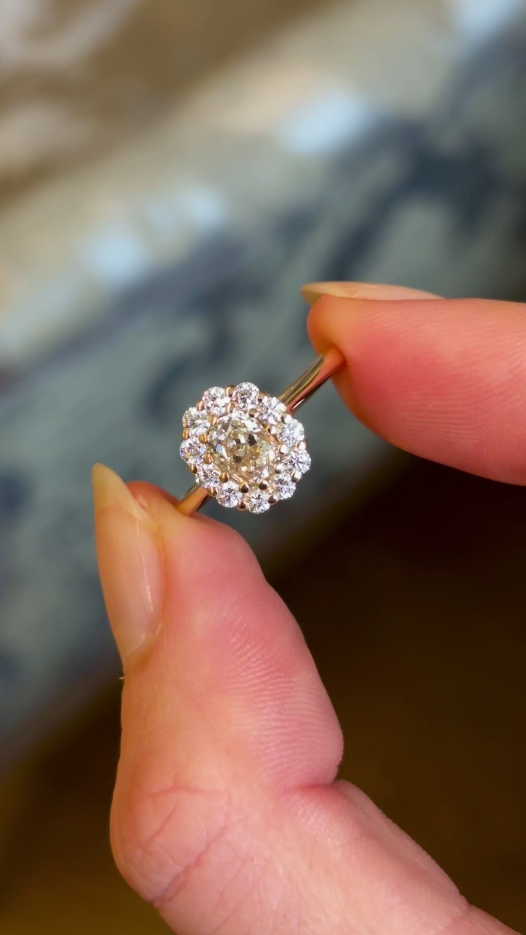 Video showing all the front and side of the yellow-brown tinted old mine-cut diamond cluster engagement ring with a vintage-inspired design, captured in natural light between two fingers