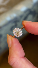 Video showing all the front and side of the yellow-brown tinted old mine-cut diamond cluster engagement ring with a vintage-inspired design, captured in natural light between two fingers