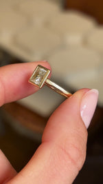 Video of a Vintage-inspired, princess-cut diamond rub-over solitaire engagement ring in yellow gold held between two fingers and rotated to show the side profile of the ring