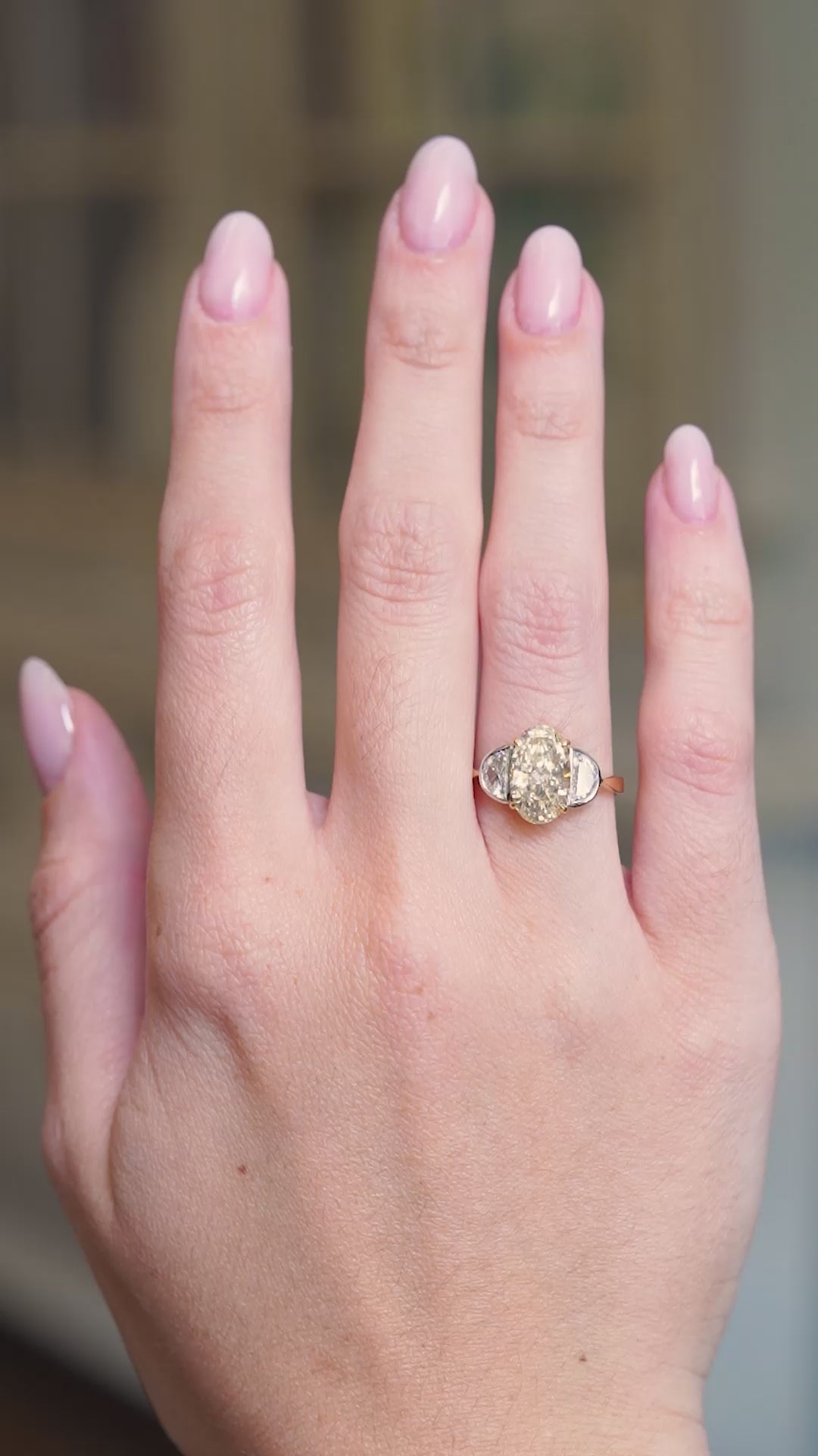 Vintage yellow oval diamond and half-moon diamond three-stone ring worn on hand shown in motion.