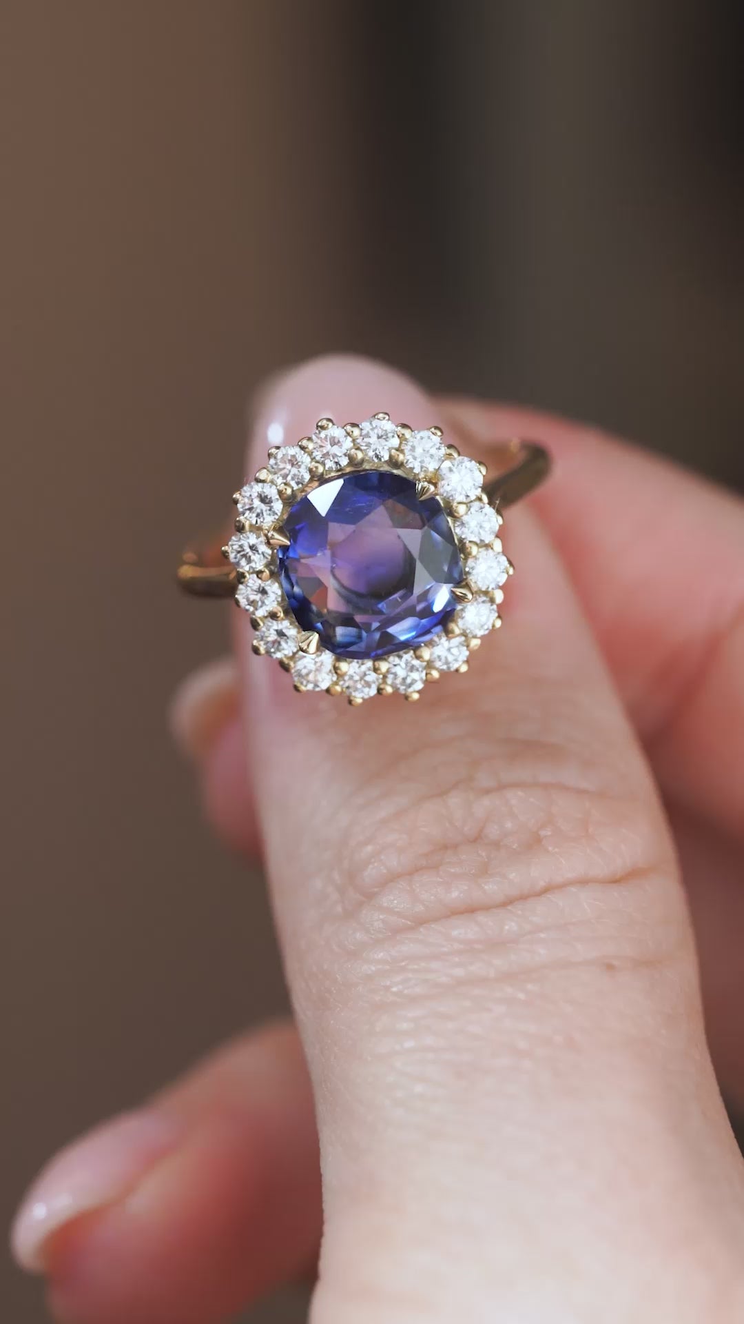 A close-up video showing the oval sapphire cluster ring balanced on a fingertip, revealing its sparkle and intricate gold claws.