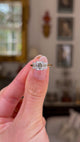 Three stone emerald-cut diamond ring, held in left hand. Rotating ring to provide full perspective, hot with antiquated bokeh background