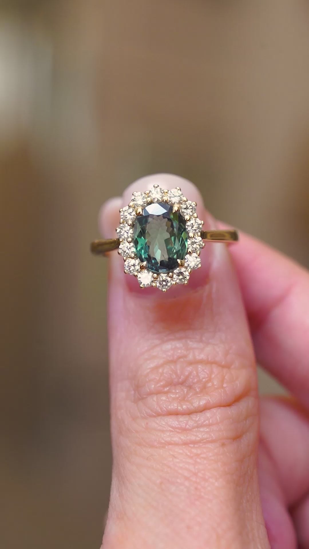 A video of two fingers holding an Antique-inspired, green colour-change alexandrite and diamond cluster engagement ring in yellow gold.  Rotating the ring to showcase it from every angle. 