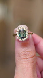 A video of two fingers holding an Antique-inspired, green colour-change alexandrite and diamond cluster engagement ring in yellow gold.  Rotating the ring to showcase it from every angle. 