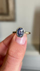 Close-up video of an antique-inspired yellow gold sapphire solitaire ring showcasing an oval-cut slate blue sapphire in a polished rub-over setting, highlighting its unique colour and elegant simplicity.