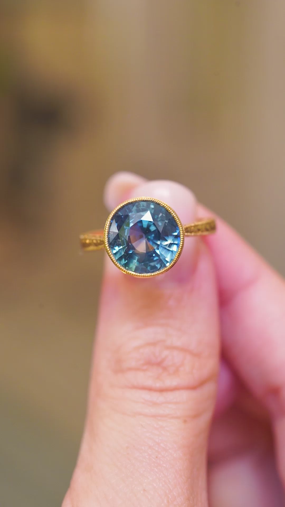 An antique-inspired, Caribbean blue sapphire solitaire ring in yellow gold with intricate detailing in the band.