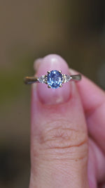 A video of a vintage-inspired blue sapphire and diamond three-stone engagement ring held between the fingers.