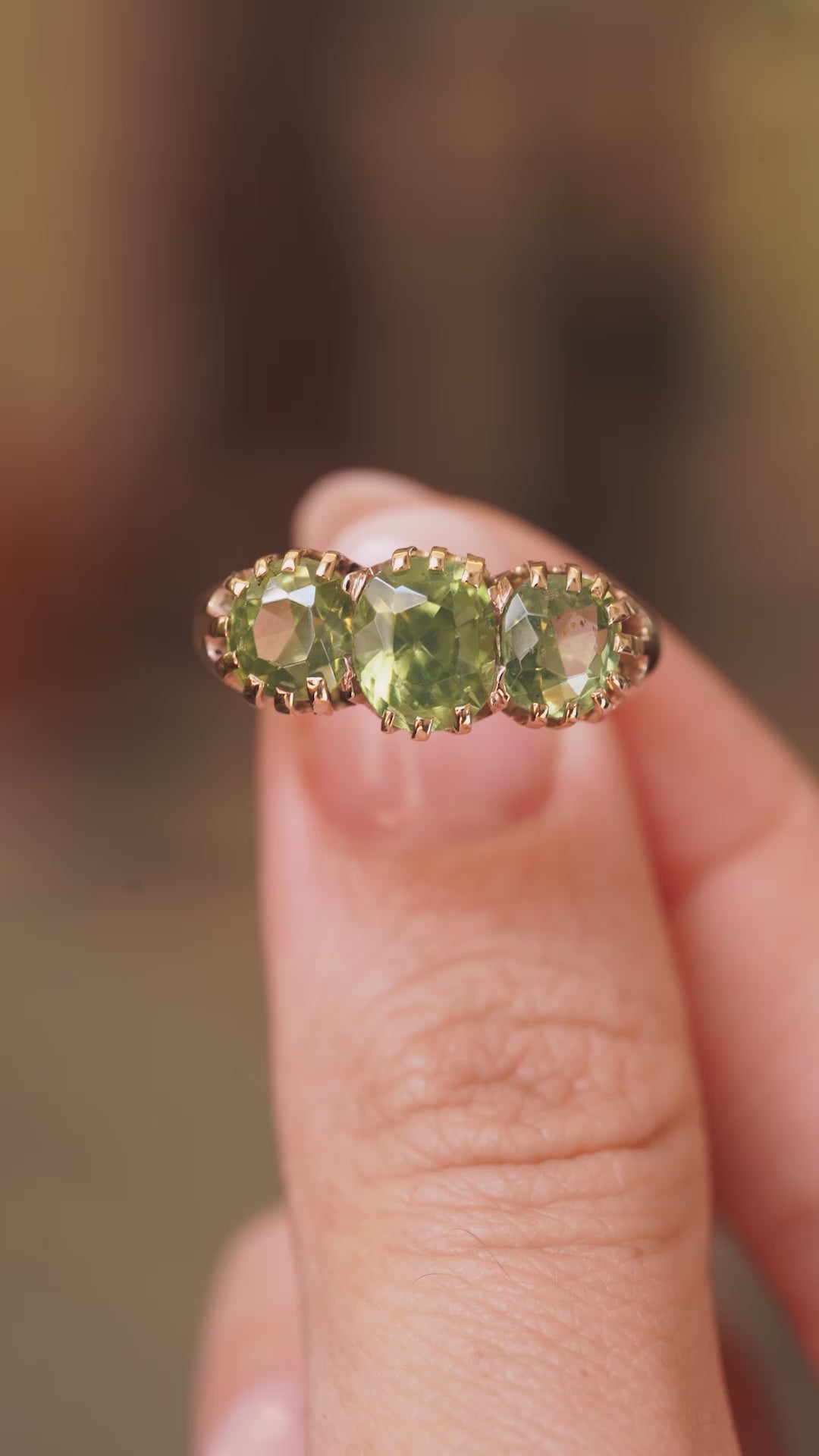 A video of a green zircon three-stone ring in gold metal held between the fingers and turned to show different angles of the ring.